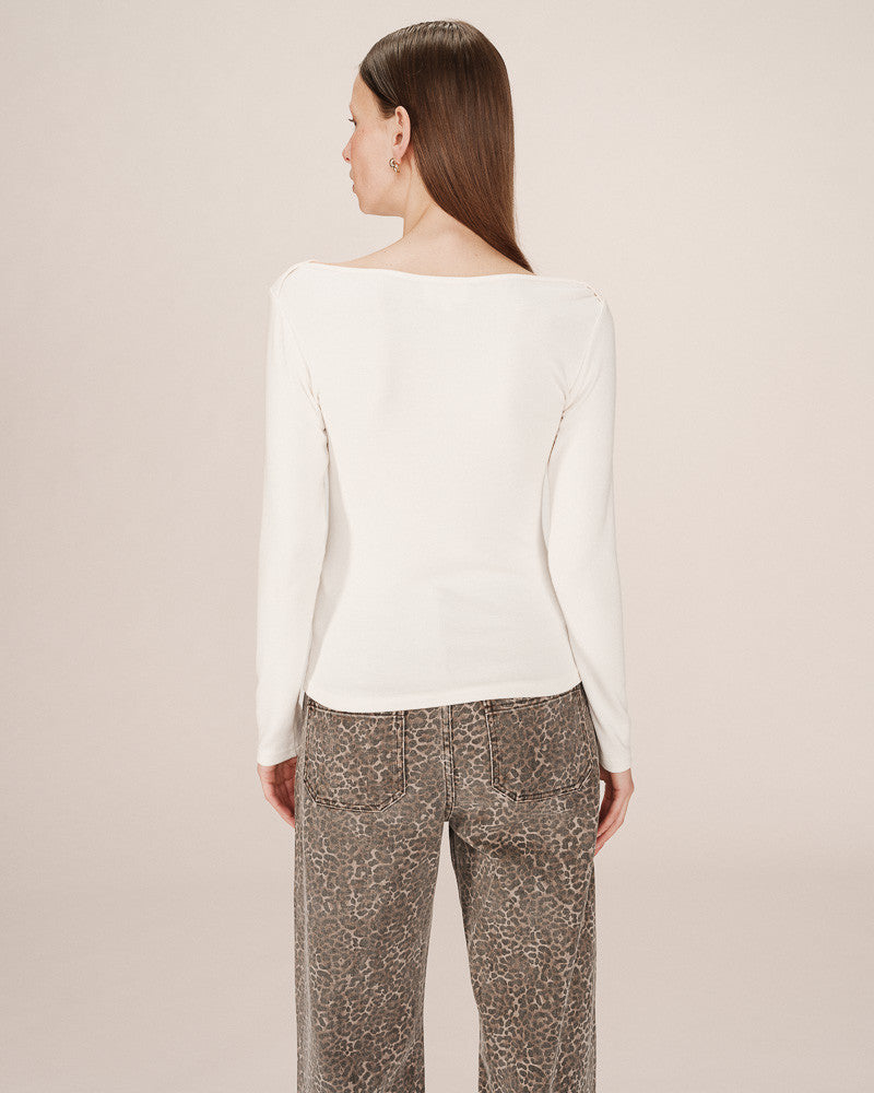 Woman wearing a white sweater and patterned pants on a beige background