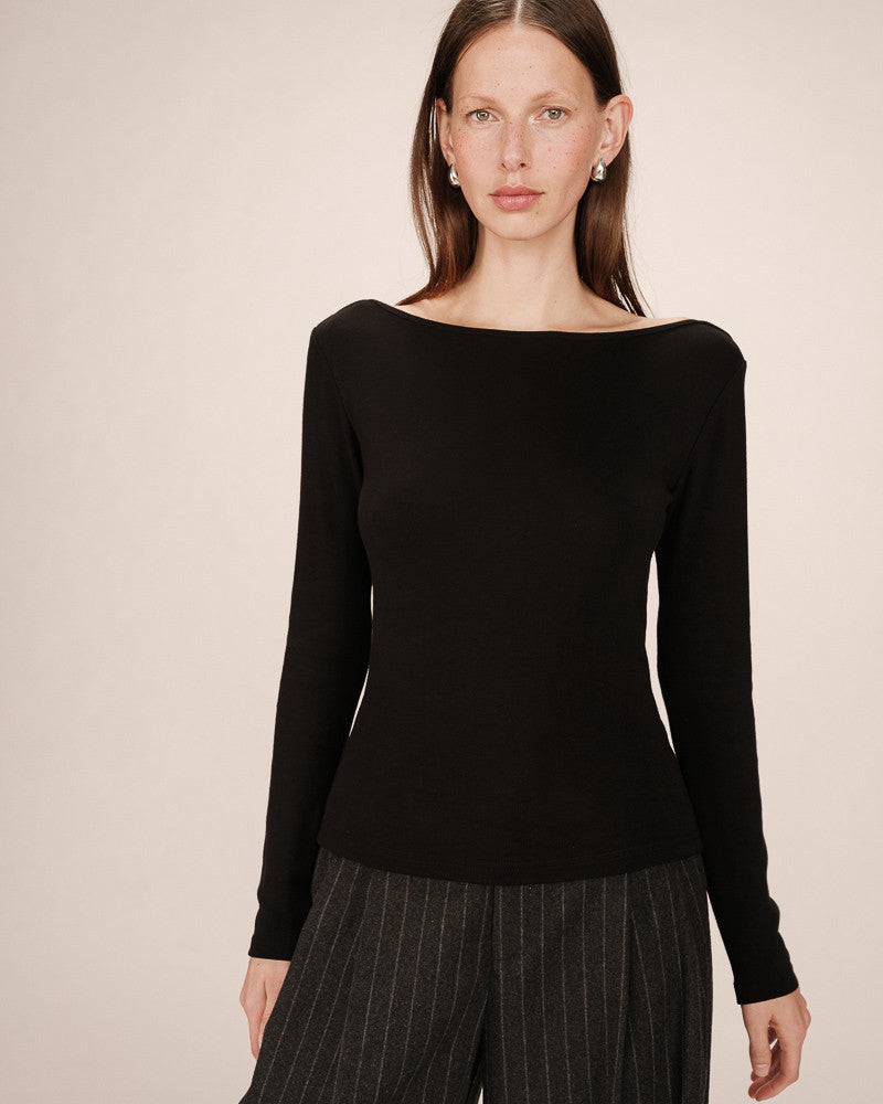 Woman wearing a black long-sleeve top against a beige background