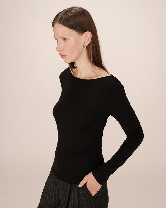 Woman wearing a black long-sleeve top against a beige background