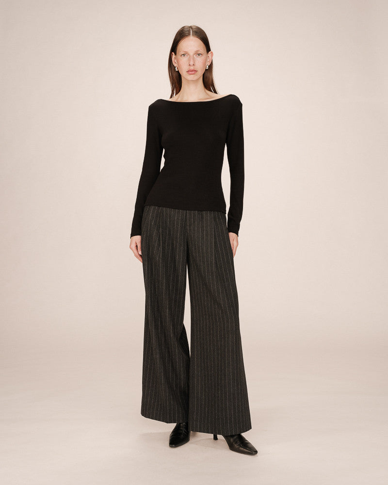 Woman wearing a black top and pinstripe pants on a beige background