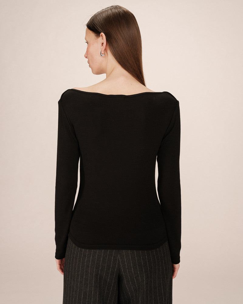 Woman wearing a black long-sleeve top with a plain background