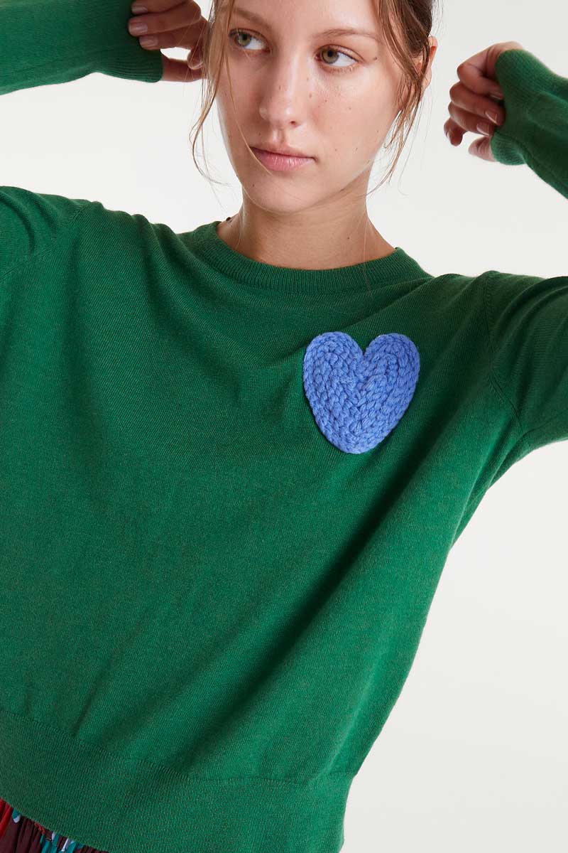 Green sweater with a blue heart patch worn by a person on a white background