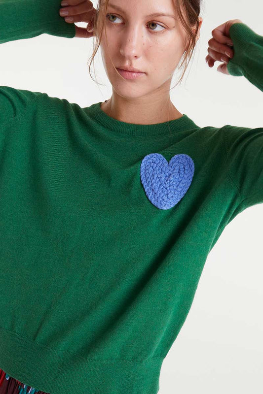 Green sweater with a blue heart patch worn by a person on a white background