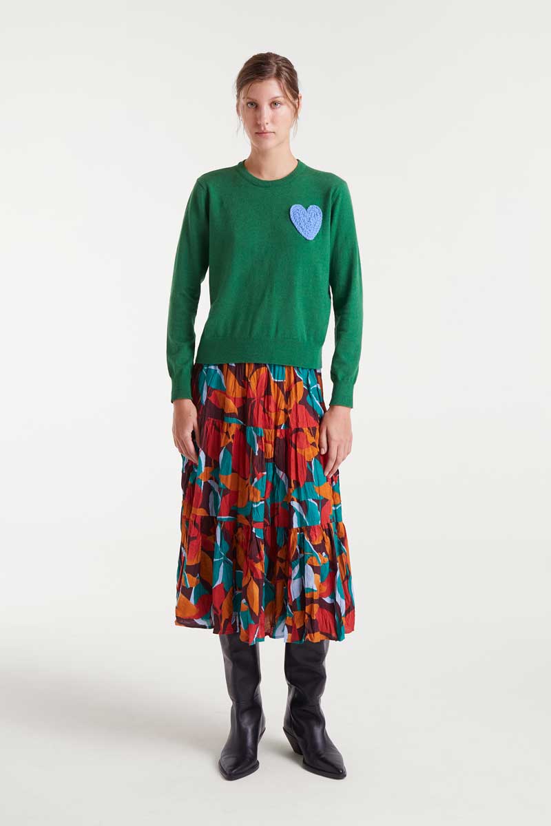 Person wearing a green sweater with a heart design and a colorful skirt on a white background