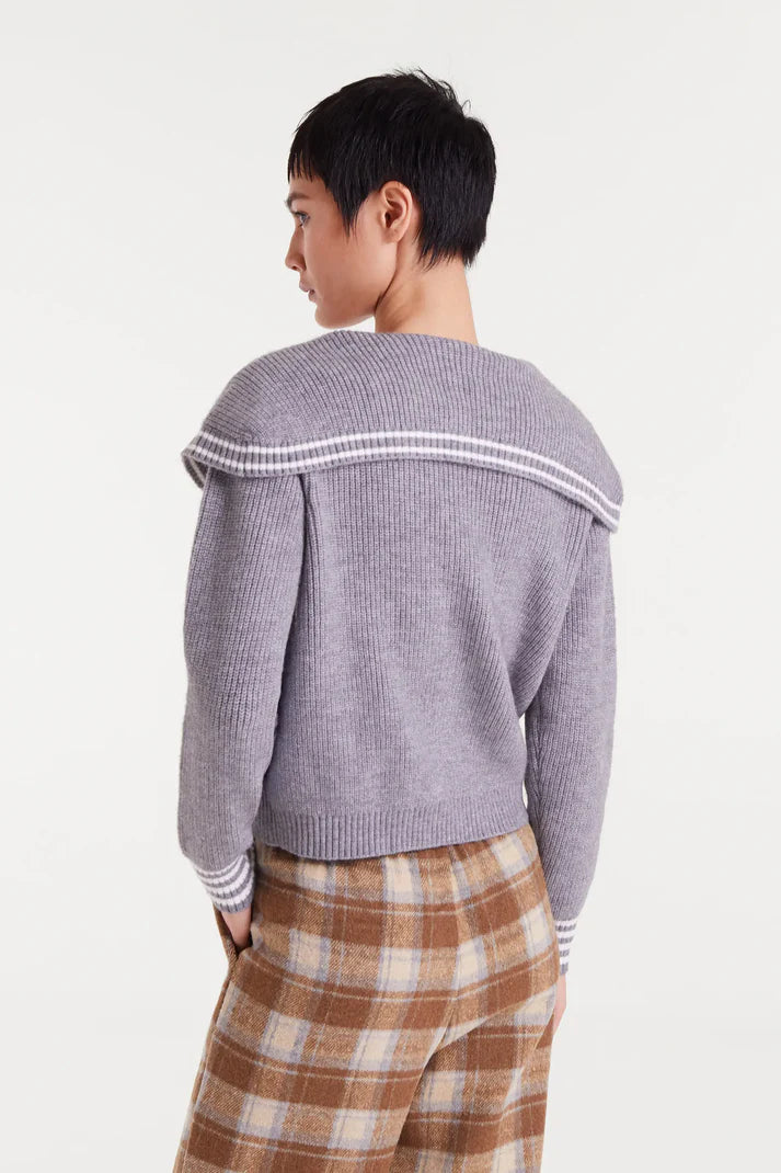 Person wearing a gray sweater with white trim and plaid pants on a white background