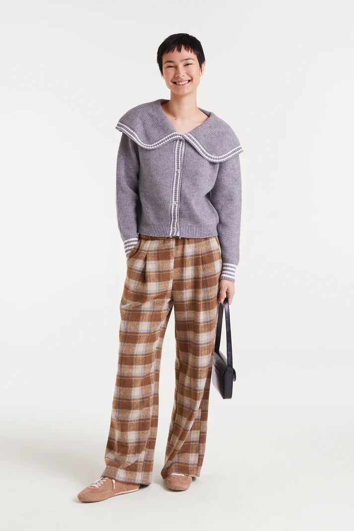 Person wearing a gray sweater with a white collar and plaid pants on a white background