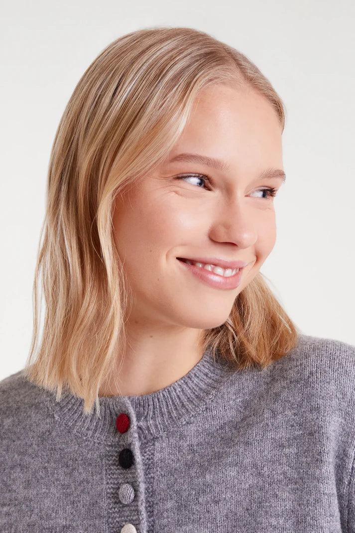 Woman with blonde hair wearing a gray sweater on a light background