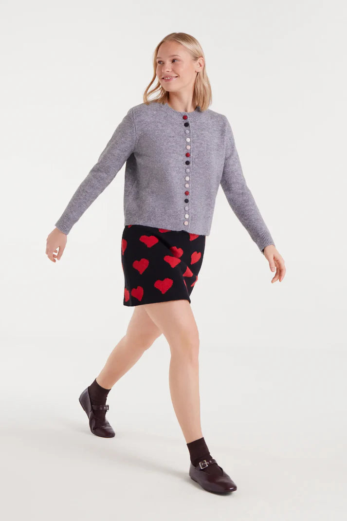 Woman wearing a gray sweater with button details and a black skirt with red heart patterns on a white background
