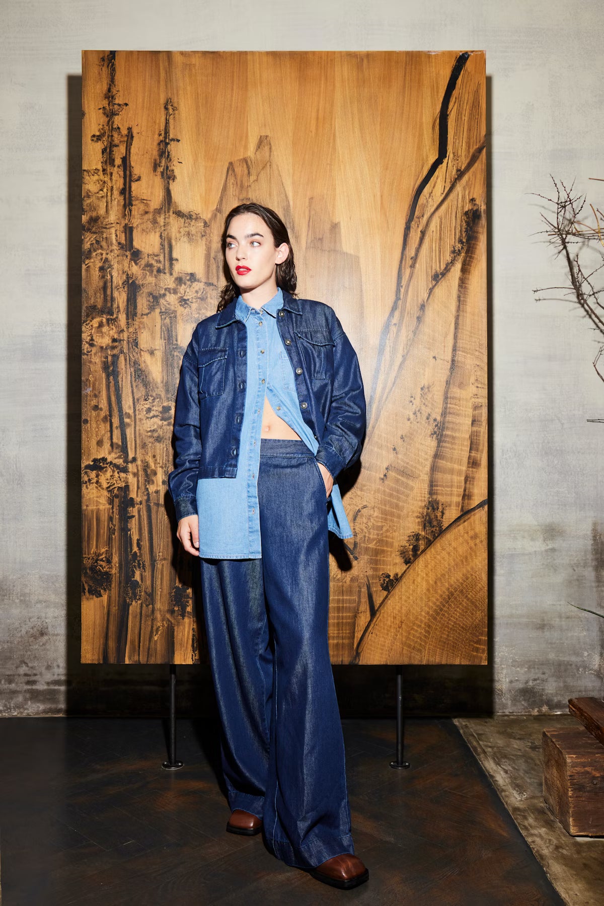 Woman in a blue denim outfit standing in front of a large wooden artwork.