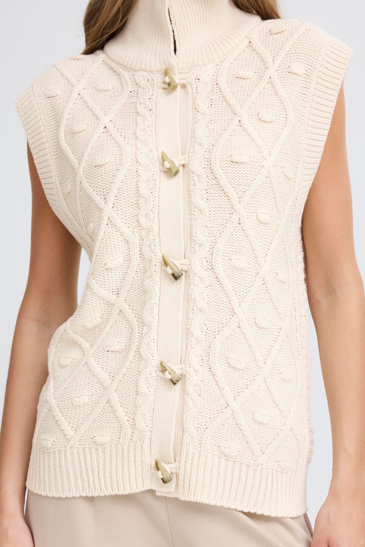 Cream-colored knitted vest with button details on a plain background