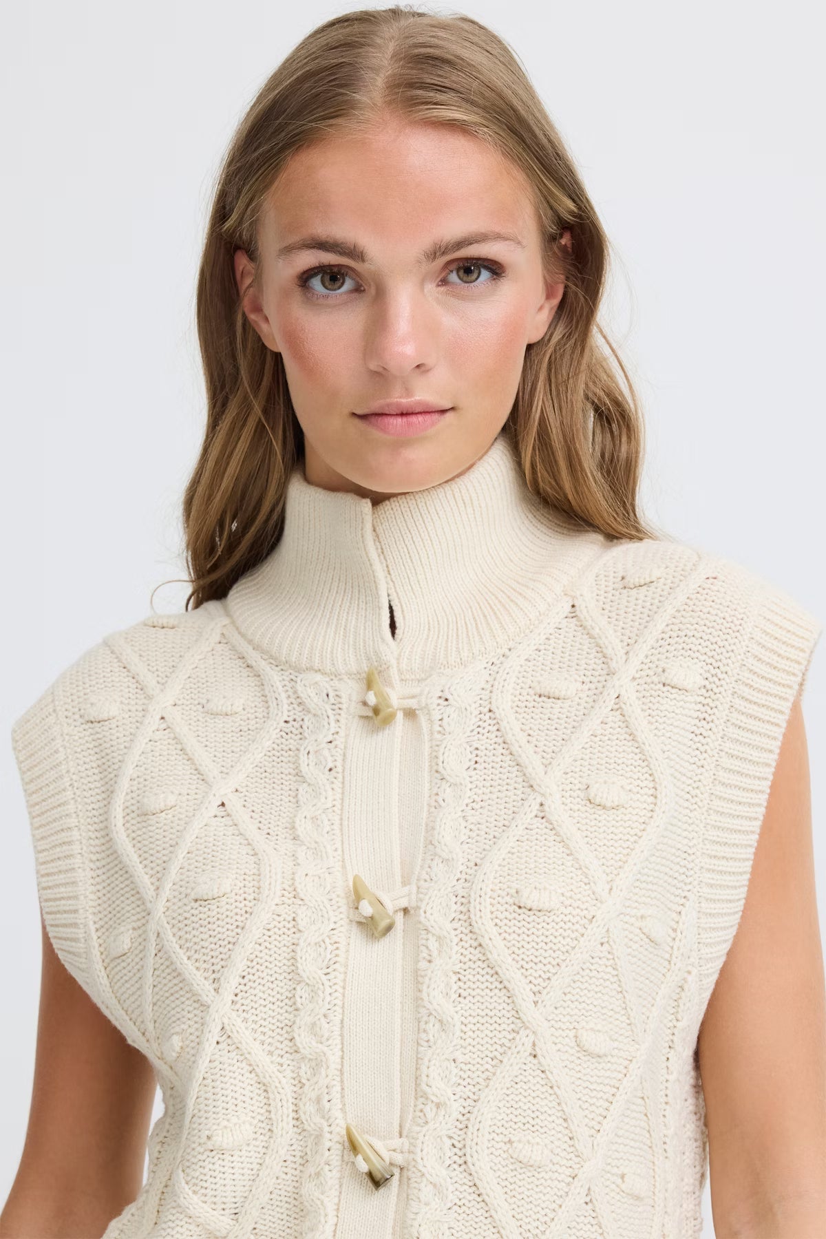 Woman wearing a cream-colored knitted vest against a white background