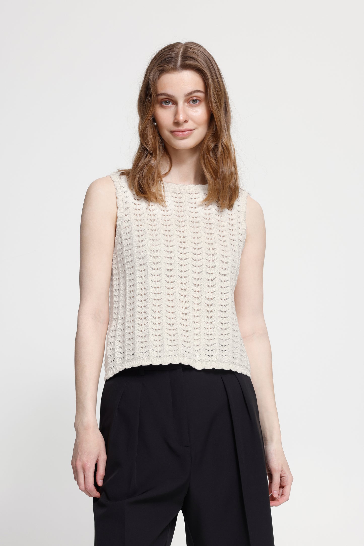 Woman wearing a sleeveless white knit top and black pants on a white background