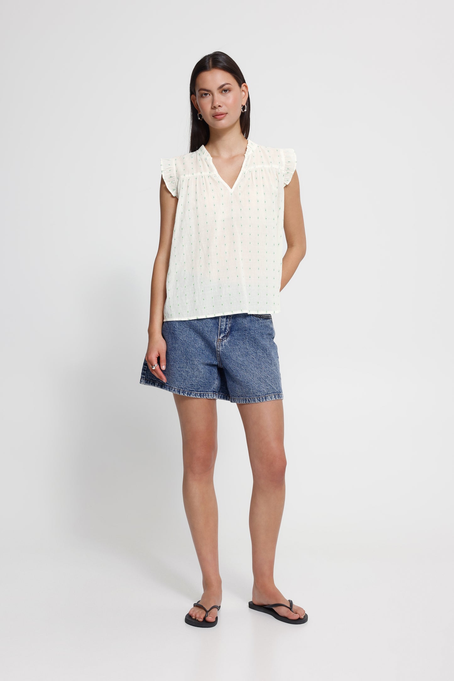 Woman wearing a white sleeveless top and denim shorts on a white background