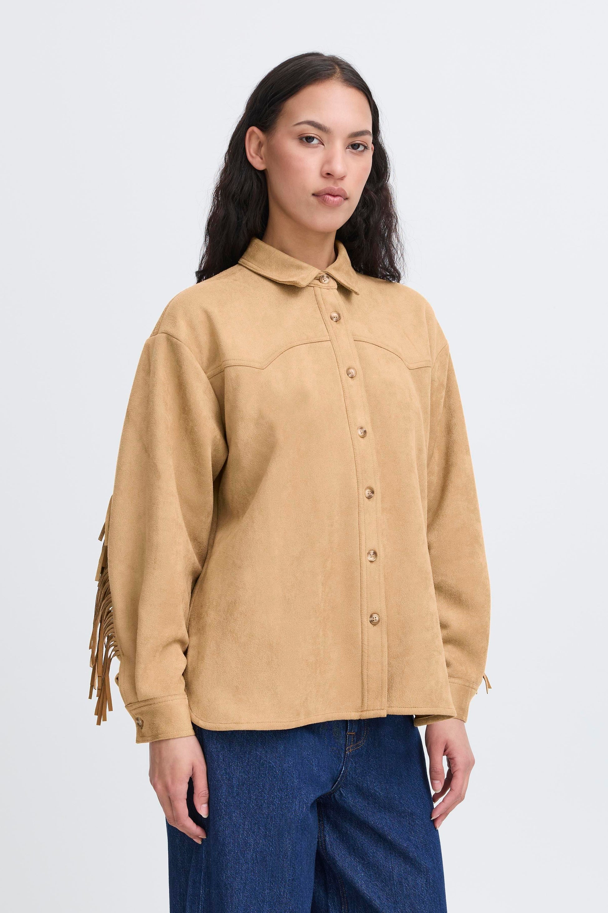 Woman wearing a beige fringed jacket and blue jeans on a white background