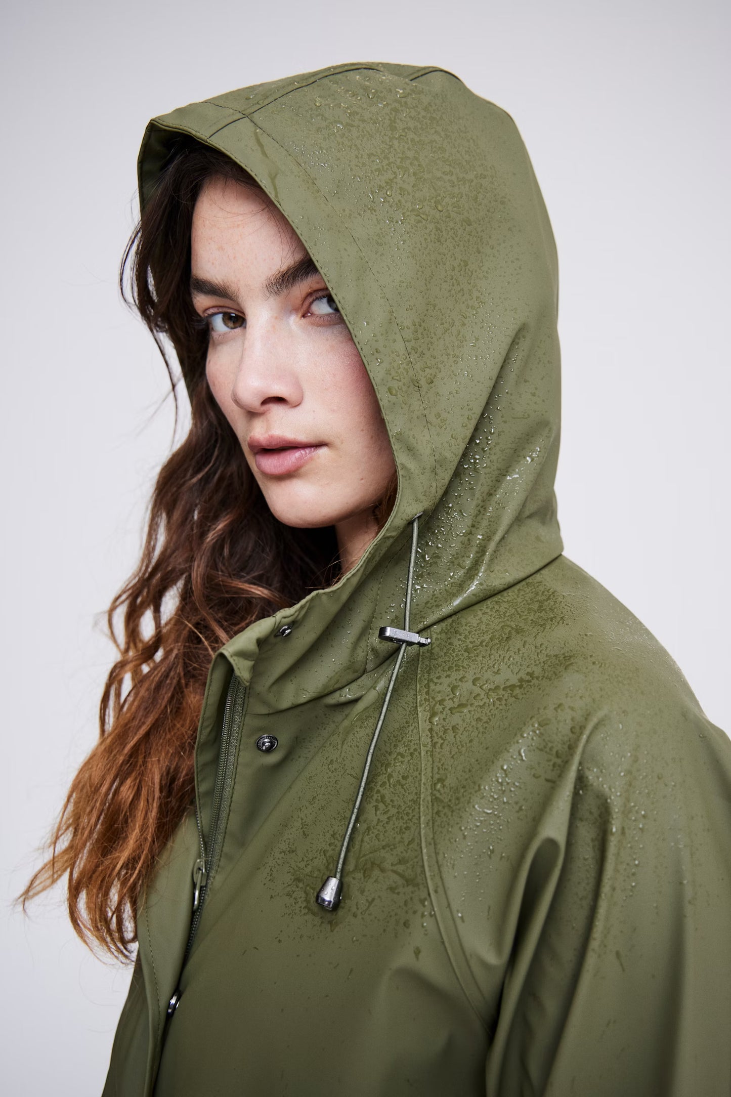 Woman wearing a green raincoat against a plain background