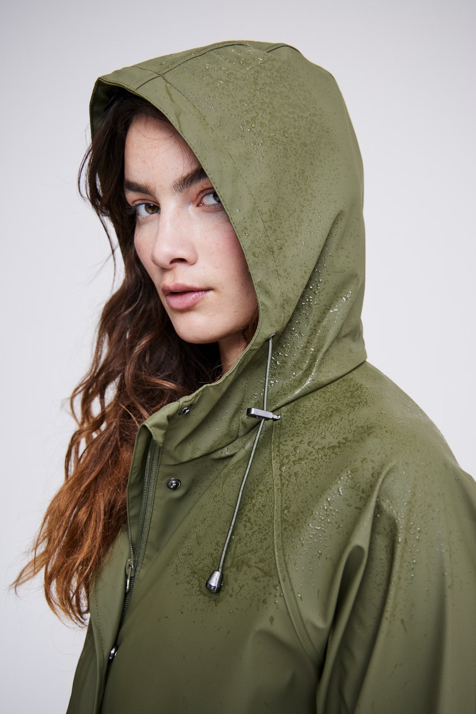 Woman wearing a green raincoat against a plain background