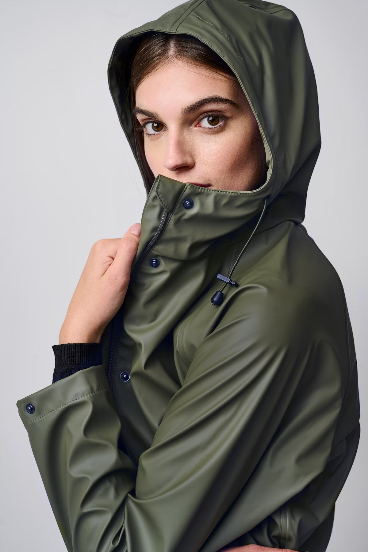 Person wearing a green raincoat with a hood on a plain background