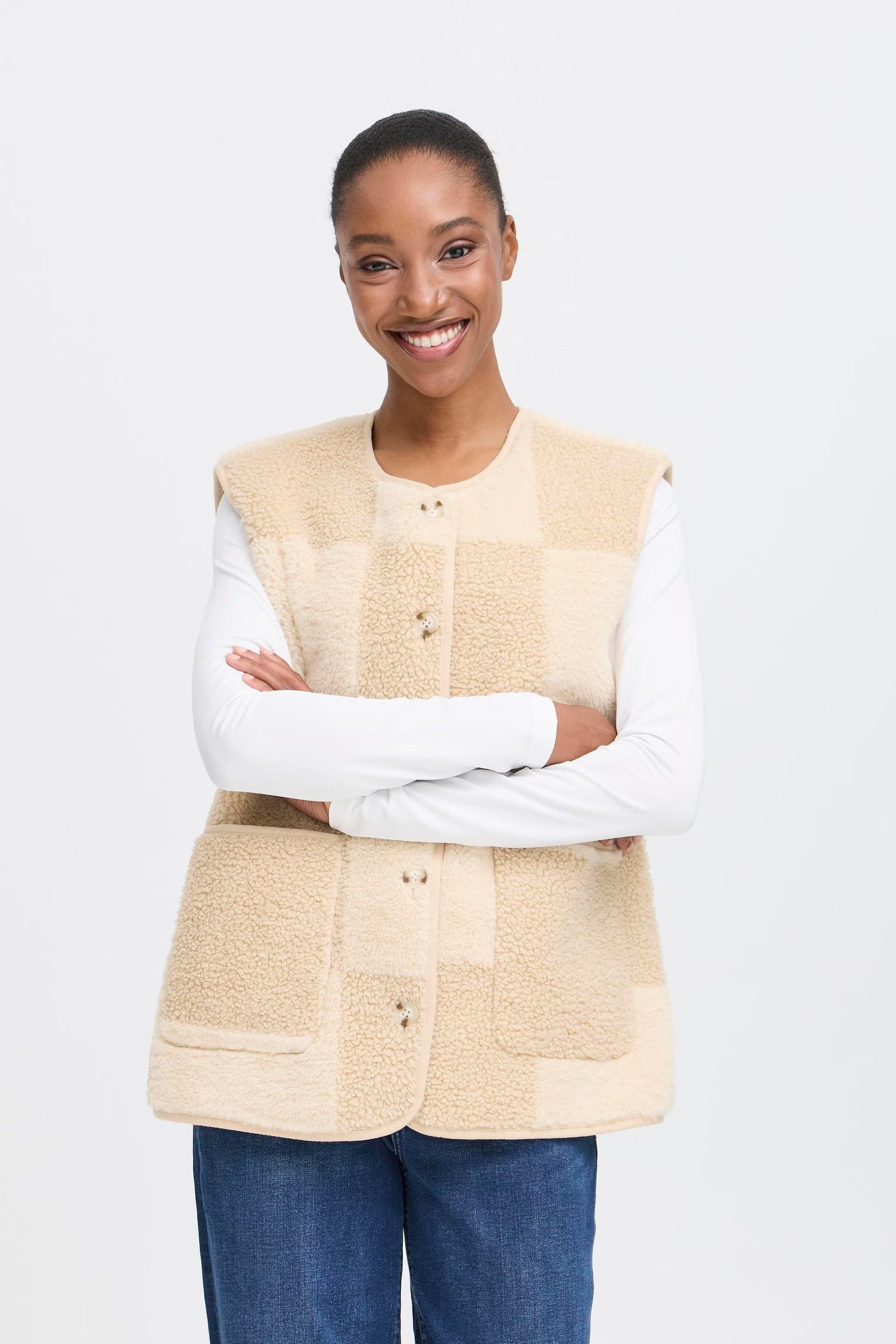 Woman wearing a beige quilted vest over a white long-sleeve shirt on a white background