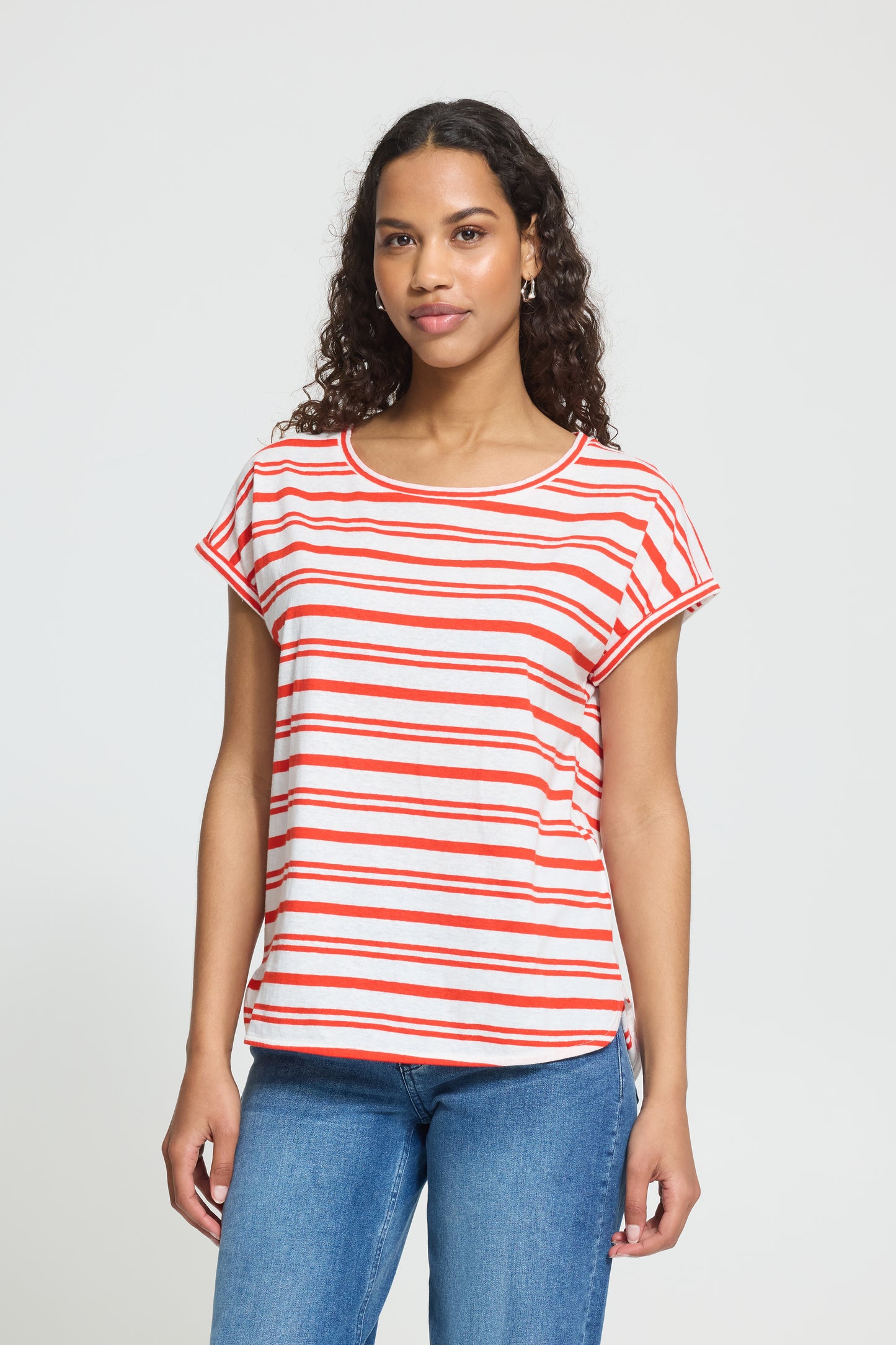 Woman wearing a red and white striped shirt with blue jeans on a light gray background