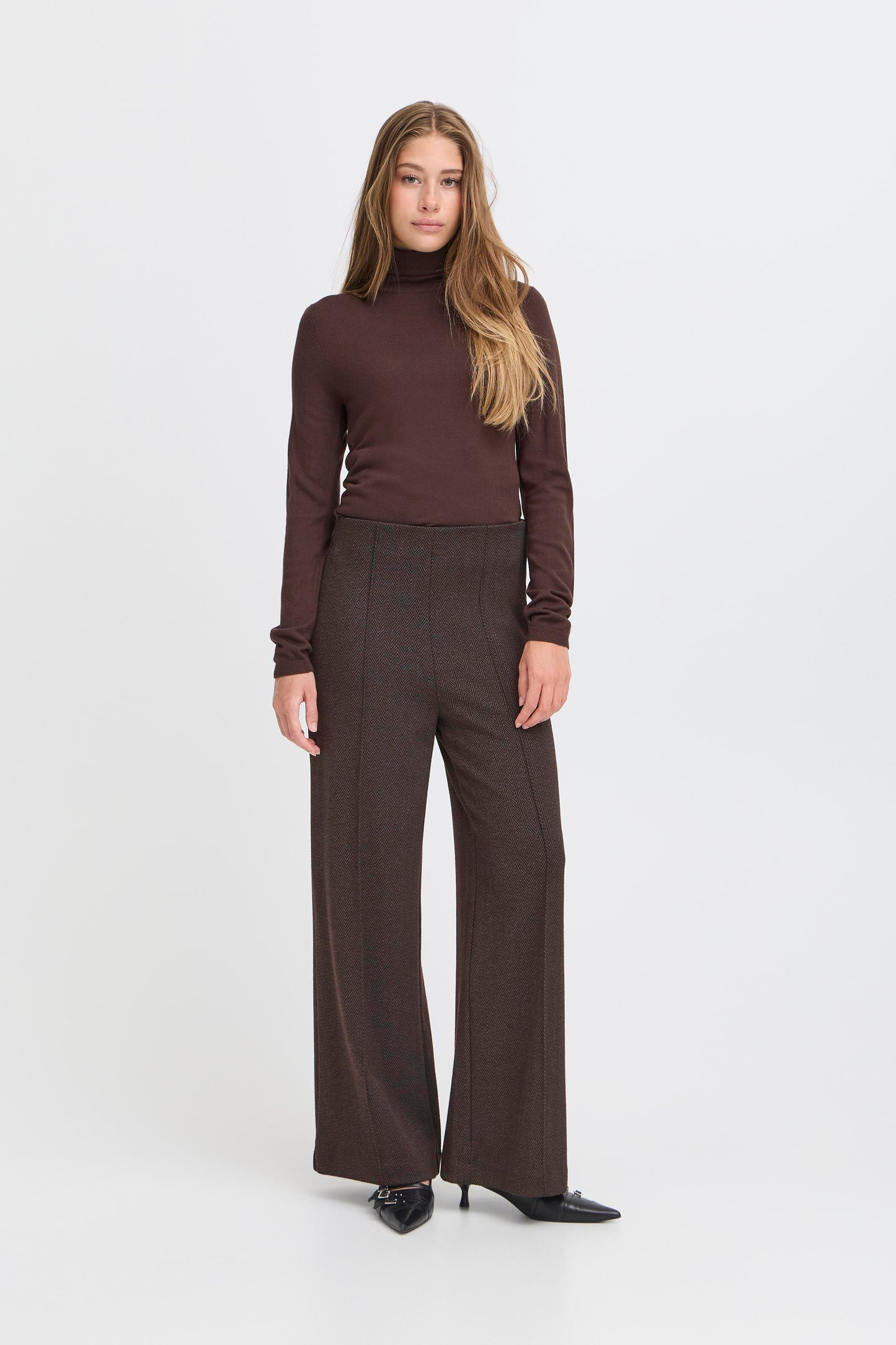 Woman wearing a brown turtleneck and wide-leg pants on a white background