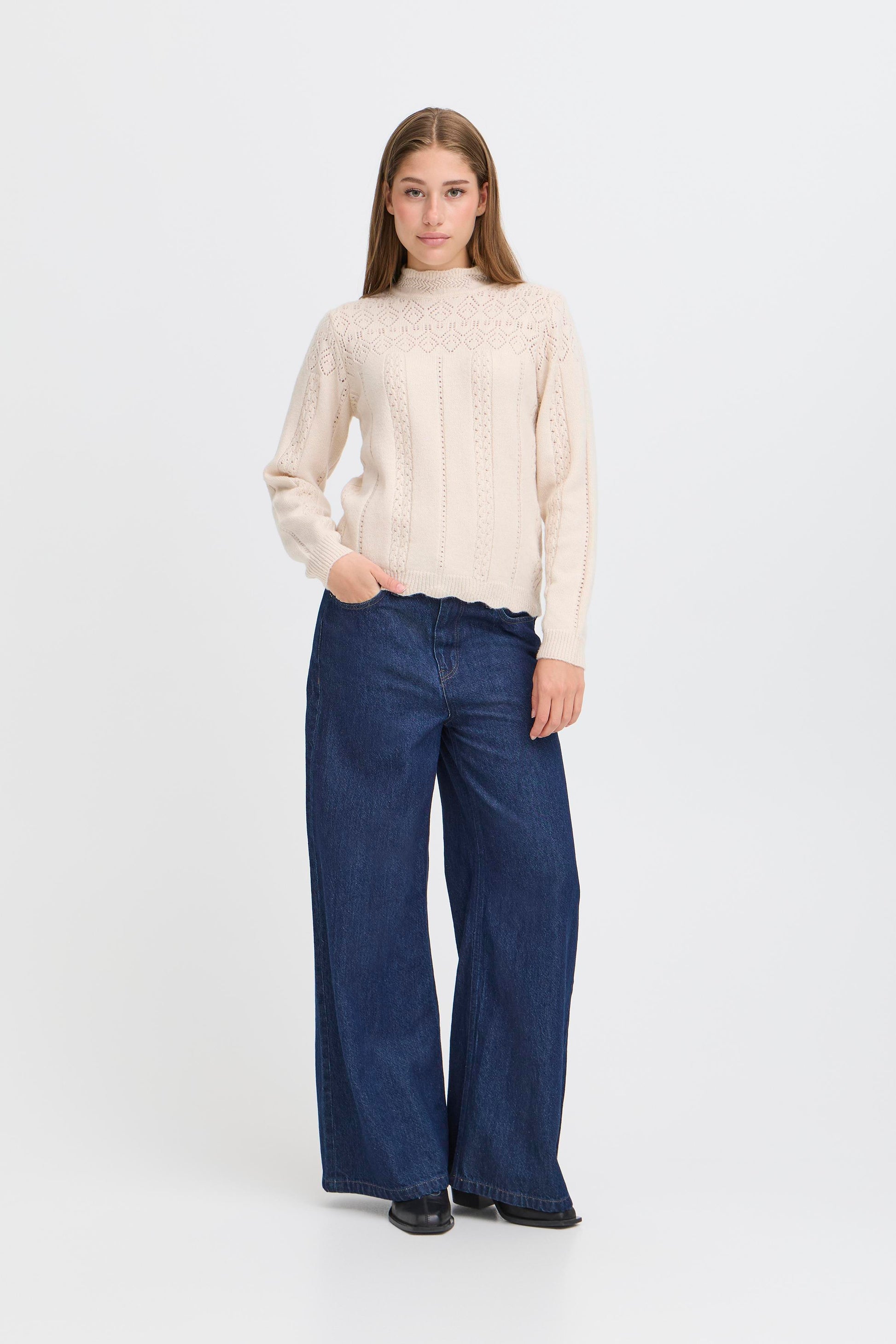 Person wearing a cream sweater and blue jeans on a white background