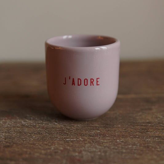 Pink ceramic cup with 'J'ADORE' text on a wooden surface