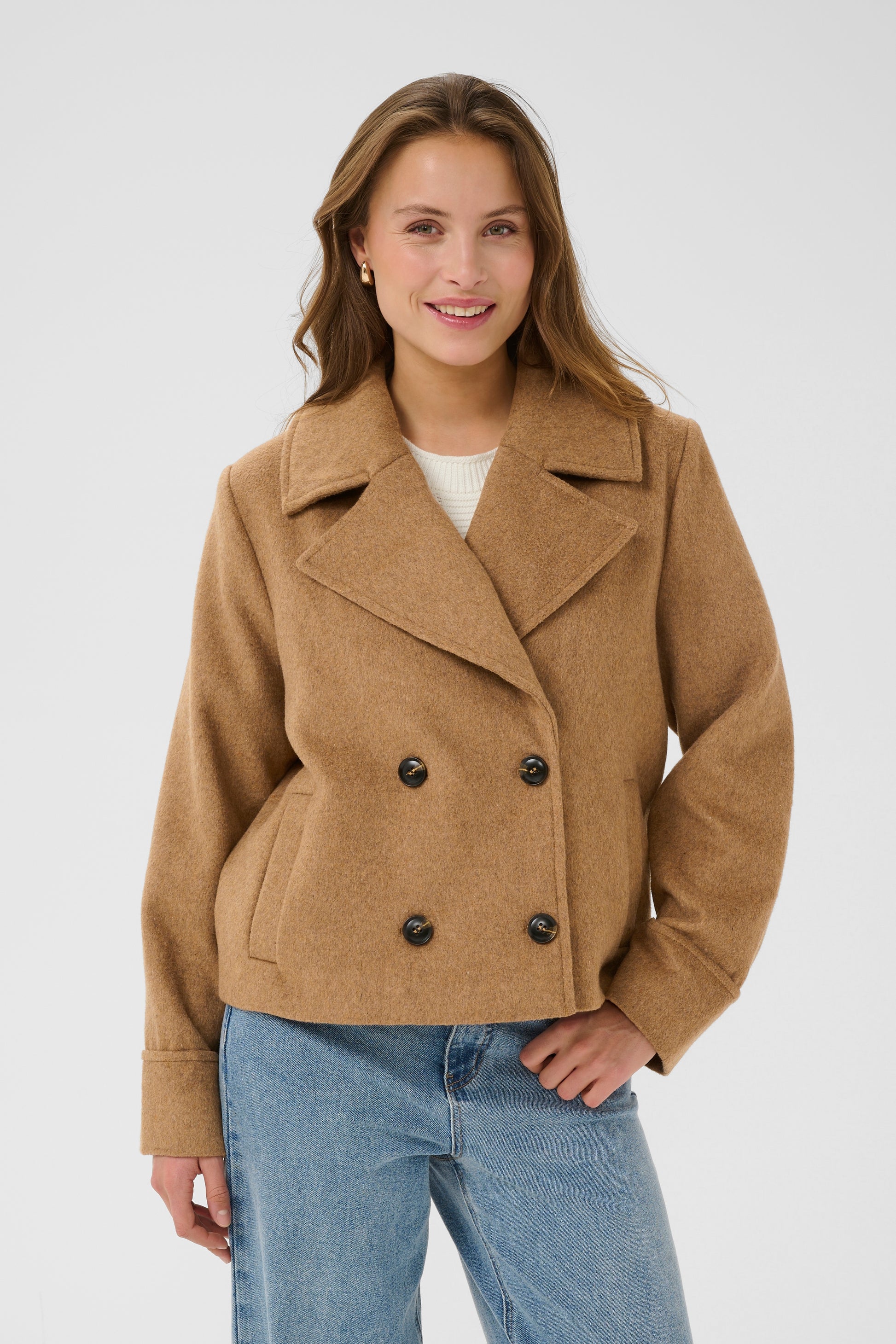 Woman wearing a brown peacoat and blue jeans on a white background