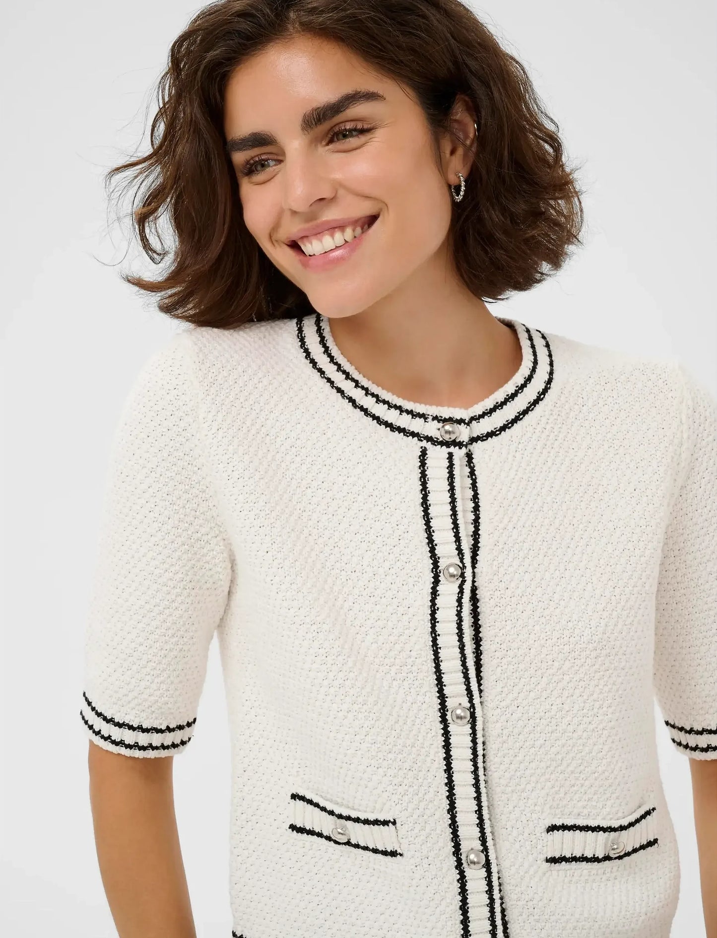Woman wearing a white tweed jacket with black trim on a light gray background