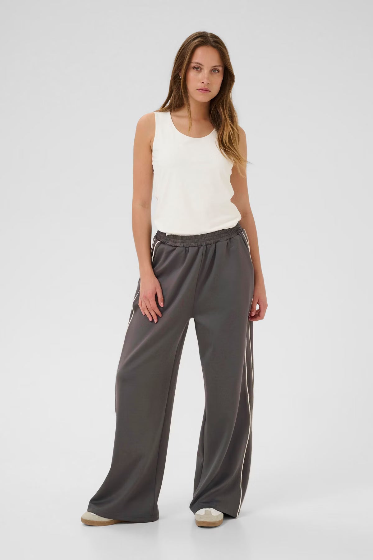 Woman wearing a white sleeveless top and gray wide-leg pants on a white background