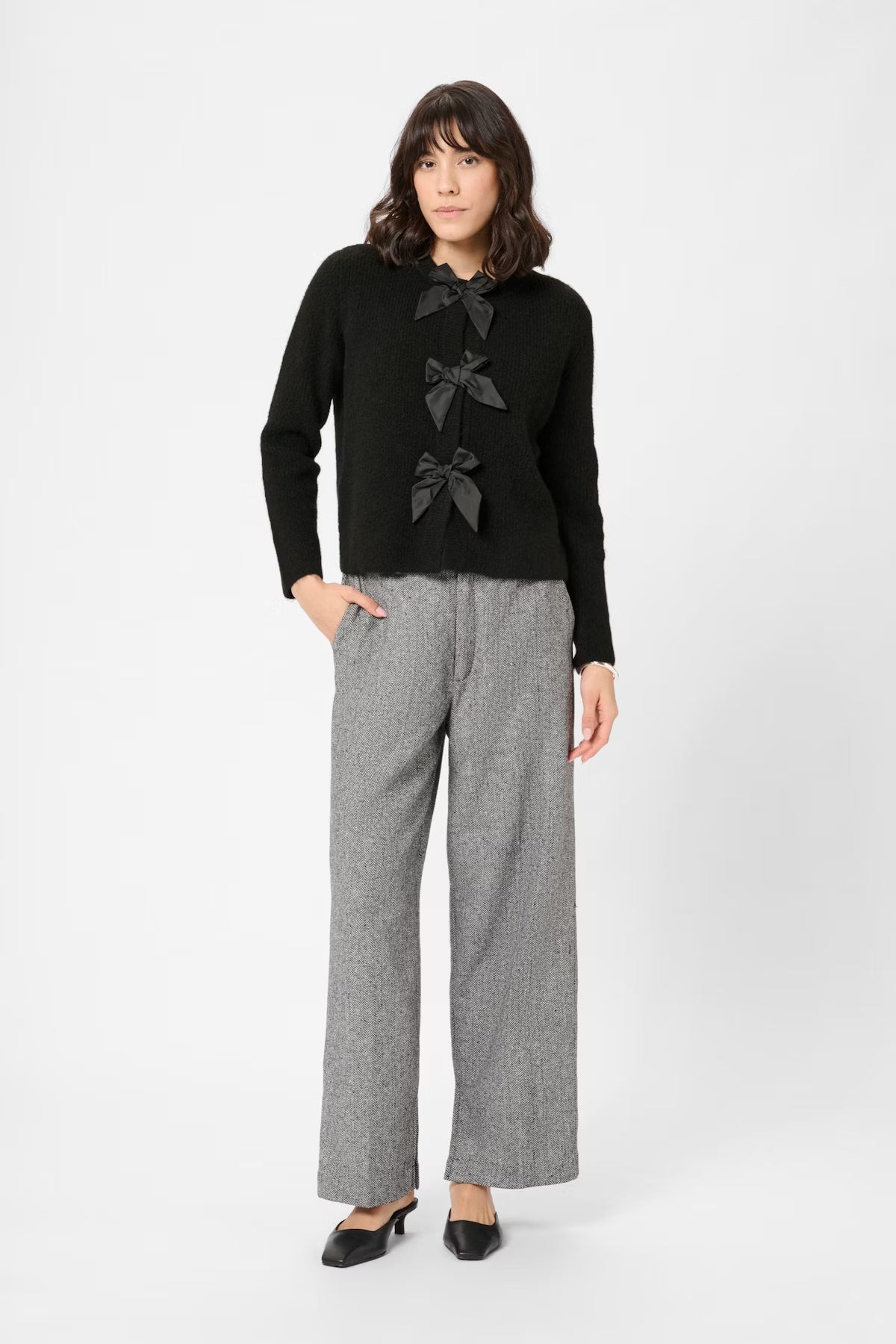 Woman wearing a black sweater with bow details and gray pants on a white background