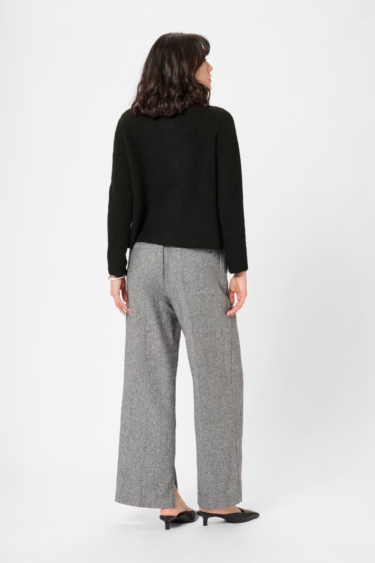 Woman wearing a black cardigan and gray pants on a white background