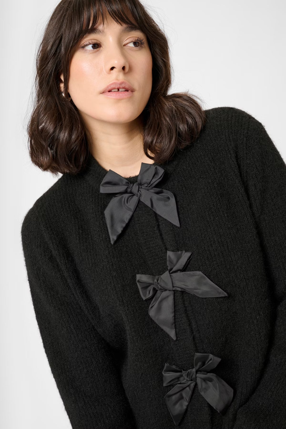 Woman wearing a black cardigan with bow details on a white background