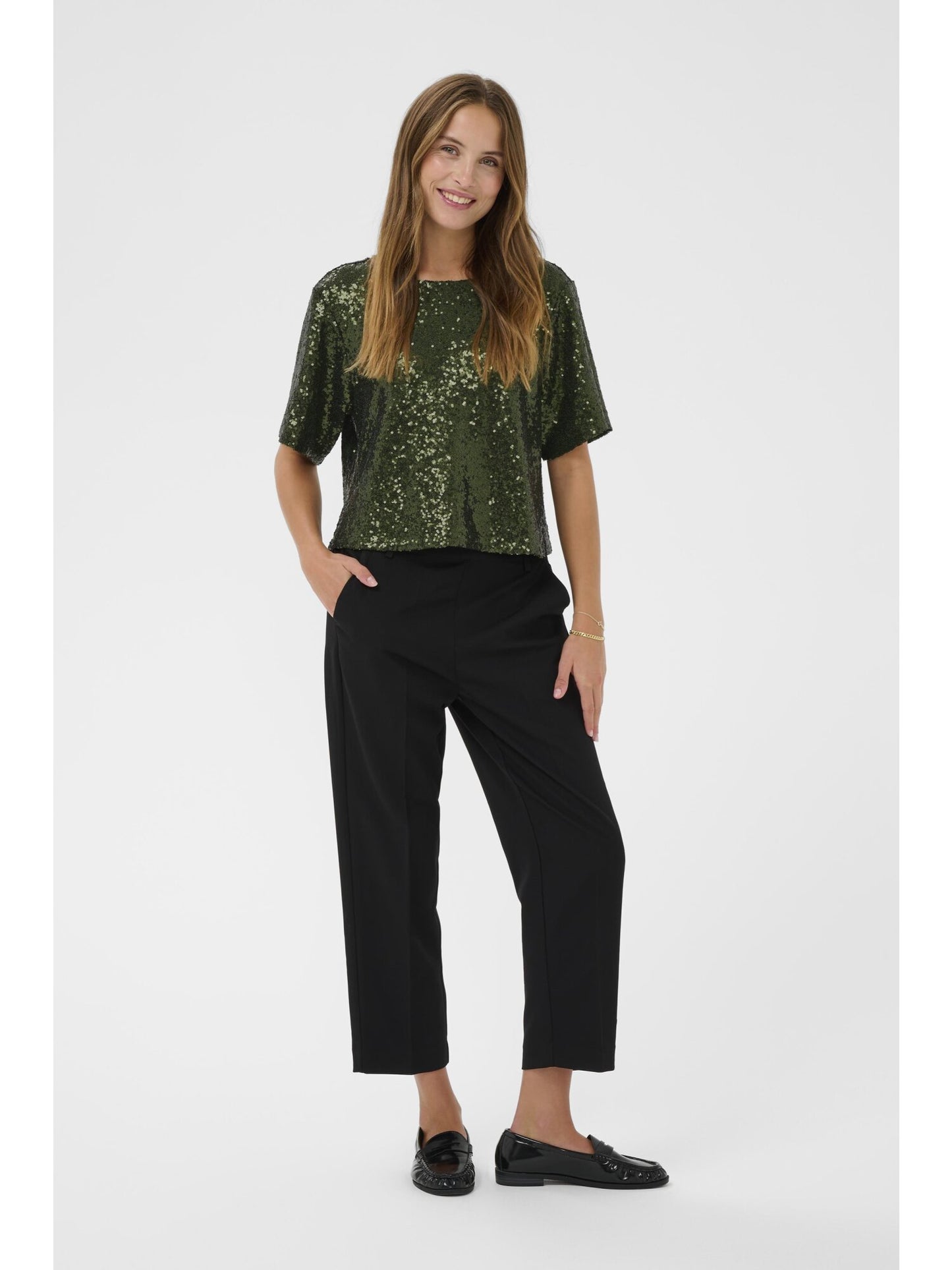 Woman wearing a green sequin top and black pants on a white background