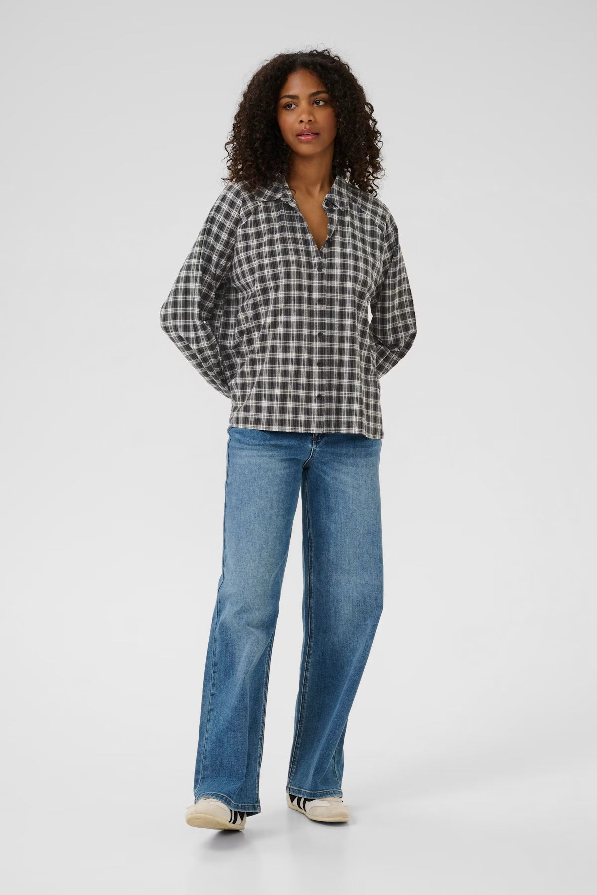 Woman wearing a checkered shirt and blue jeans on a white background