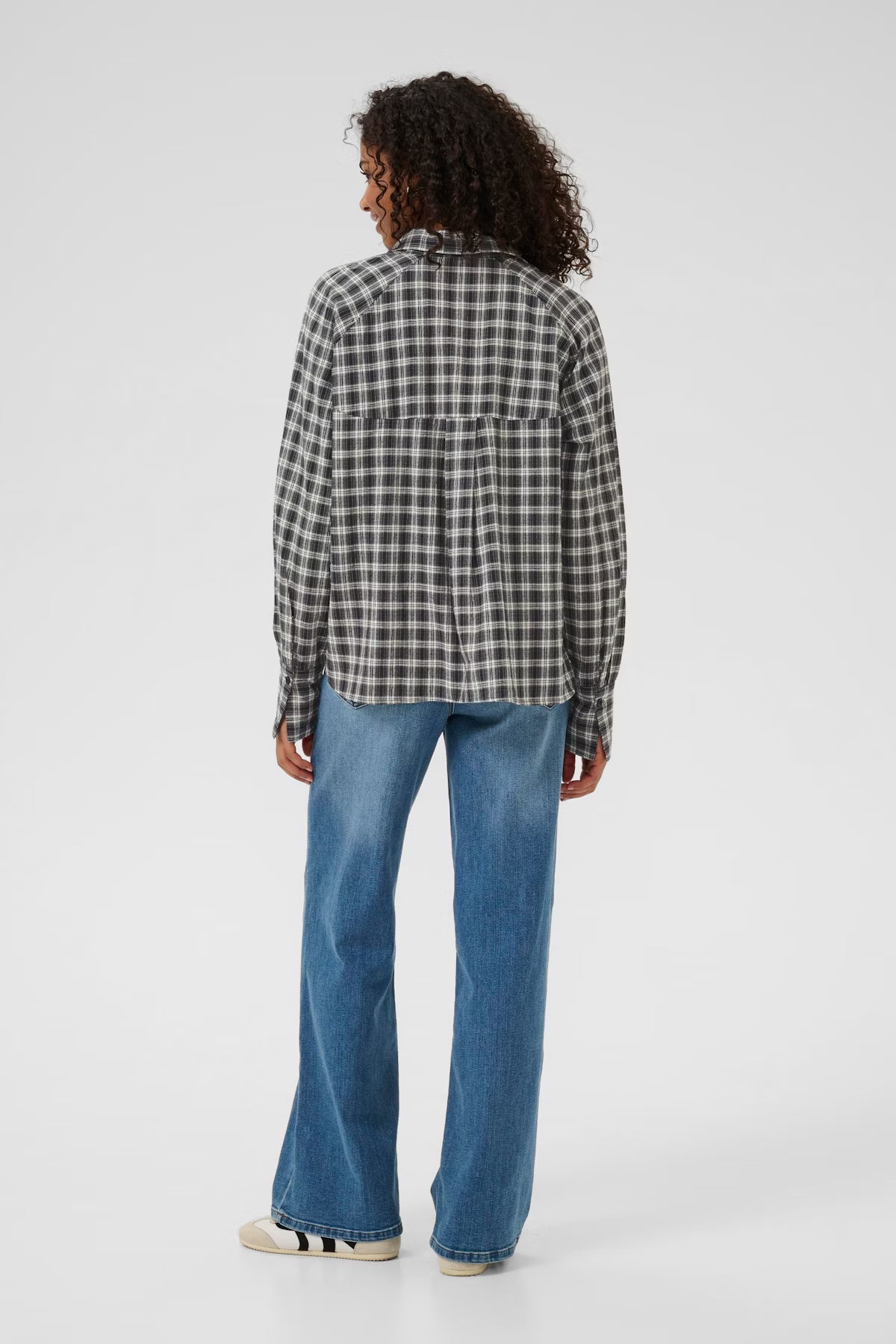 Person wearing a checkered shirt and blue jeans on a white background