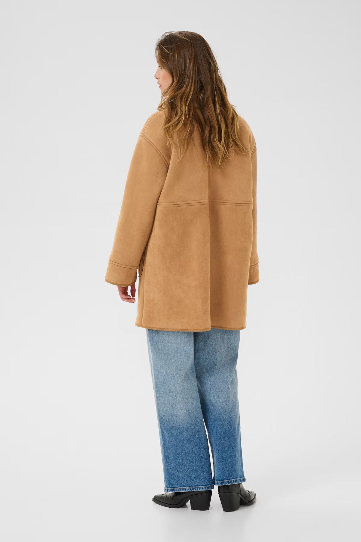 Person wearing a tan coat and blue jeans on a white background