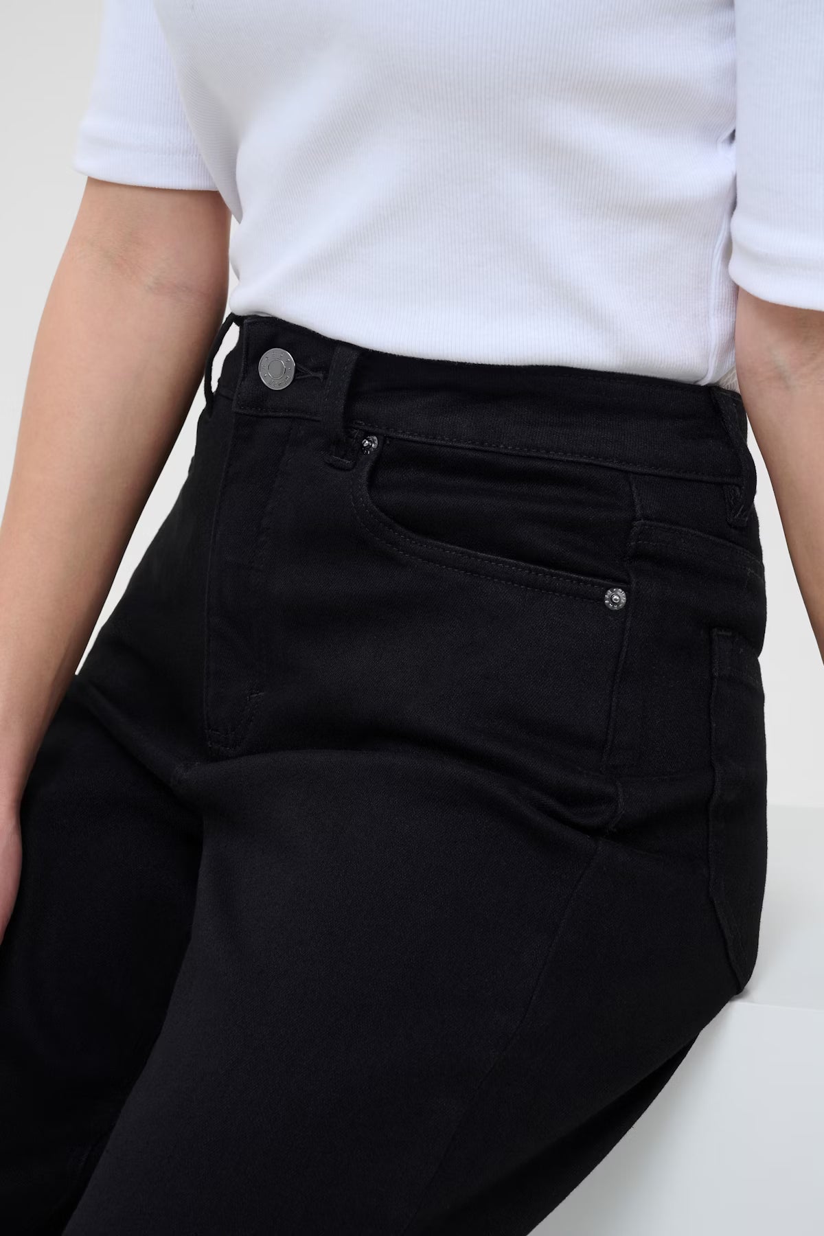 Person wearing black jeans and a white shirt on a plain background