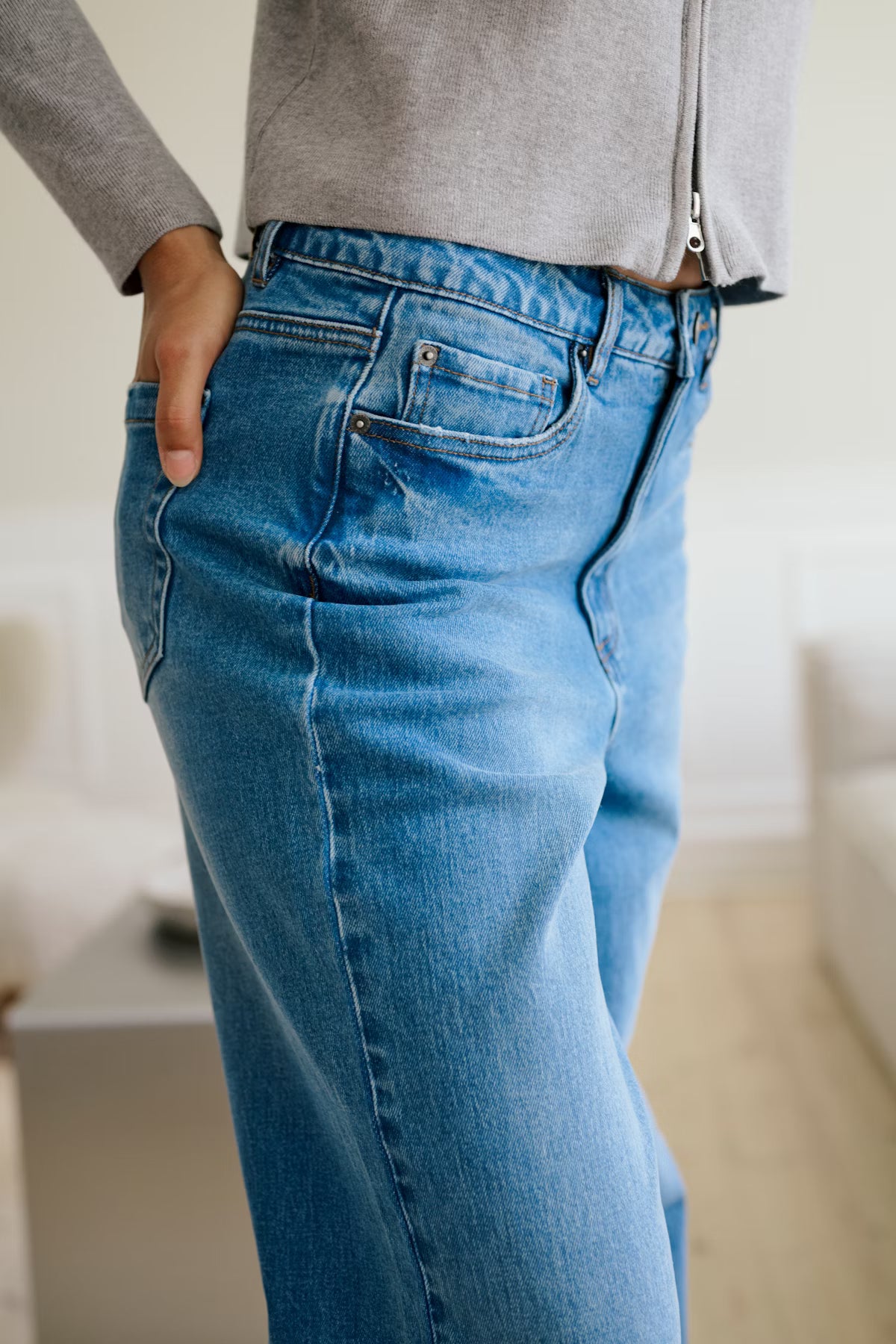 Person wearing blue jeans and a gray sweater in an indoor setting