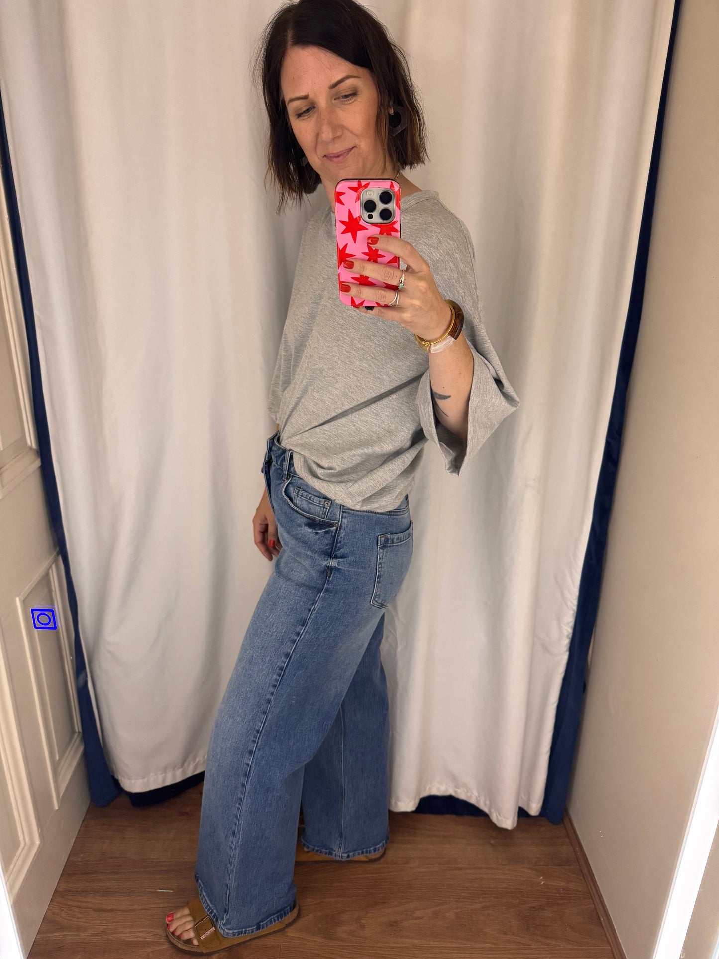 Person taking a mirror selfie wearing a gray top and blue jeans in a room.