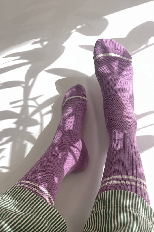 Purple socks with white stripes worn by a person, standing on a light surface with plant shadows.