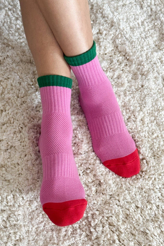 Pink socks with green cuffs and red toes on a light carpet