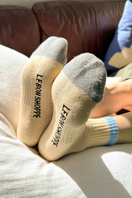 Beige socks with gray toes and 'LE BON SHOPPE' branding on a couch.
