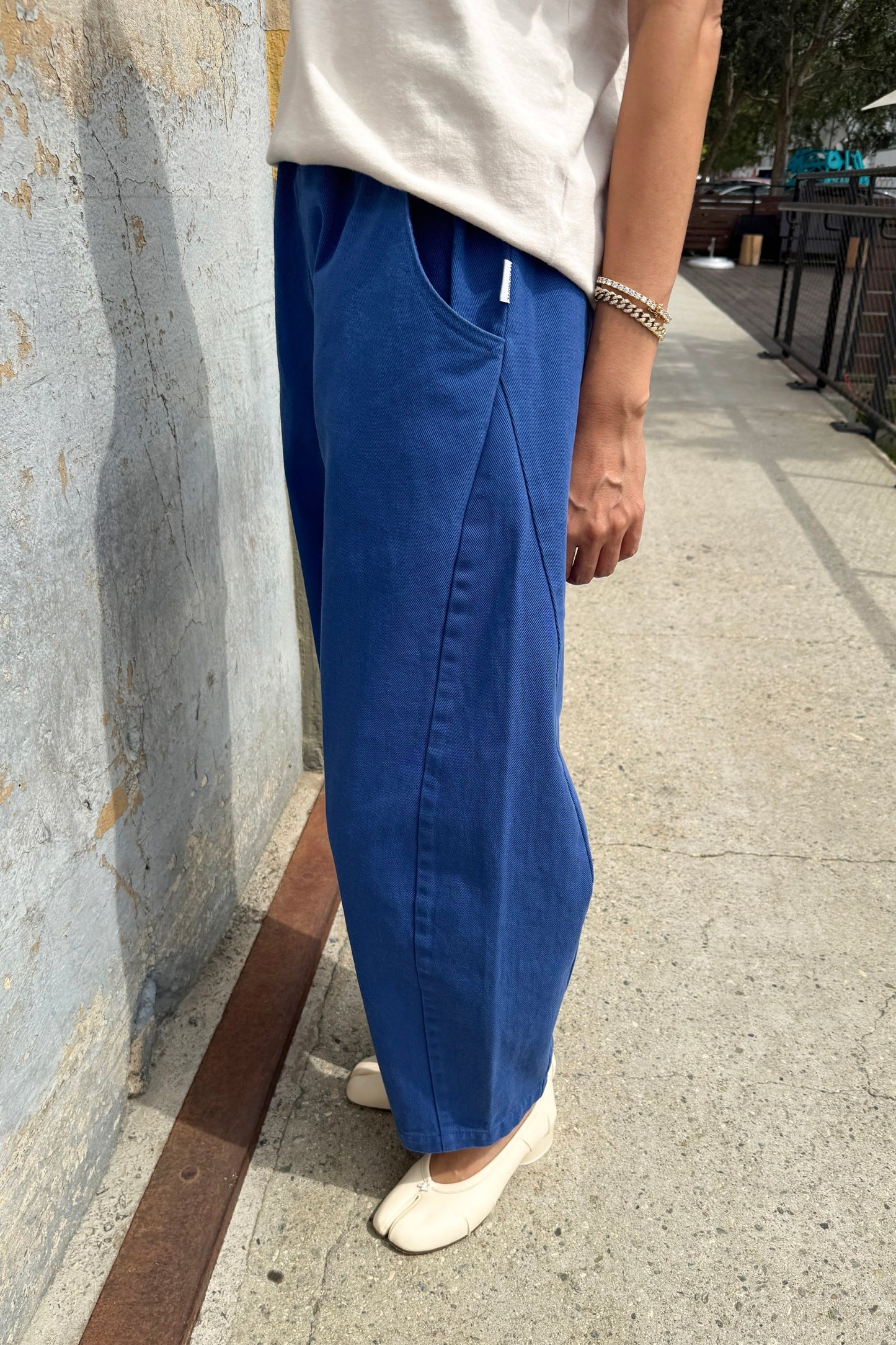 Person wearing blue pants and a white shirt standing on a sidewalk.