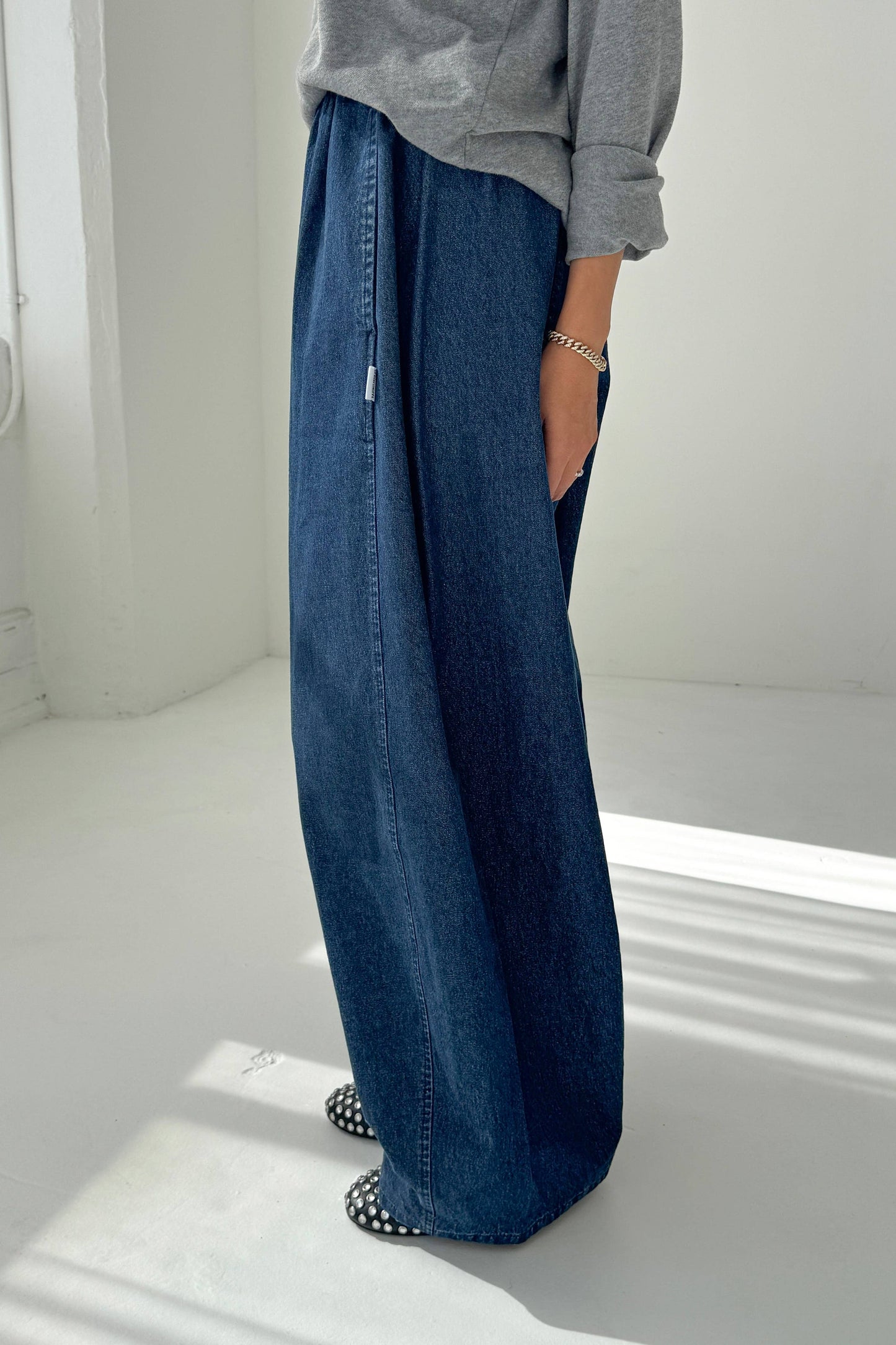 Person wearing blue wide-leg jeans and a gray top on a white background
