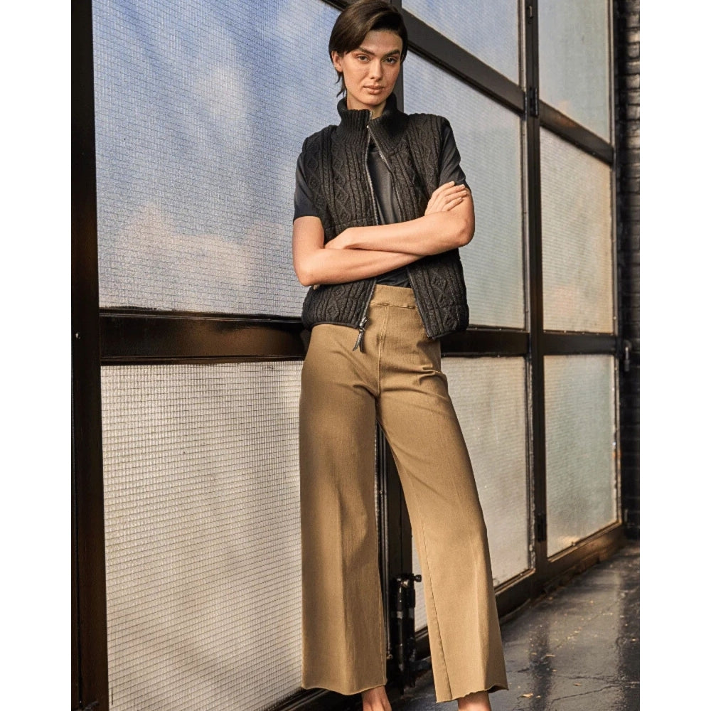 Person wearing a black jacket and beige pants standing in front of a glass wall.