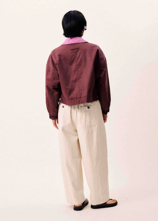 Person wearing a maroon jacket and beige pants on a white background