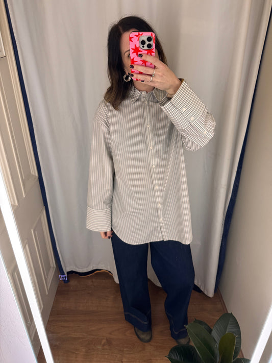 Person wearing a striped shirt and blue pants taking a mirror selfie against a white curtain.