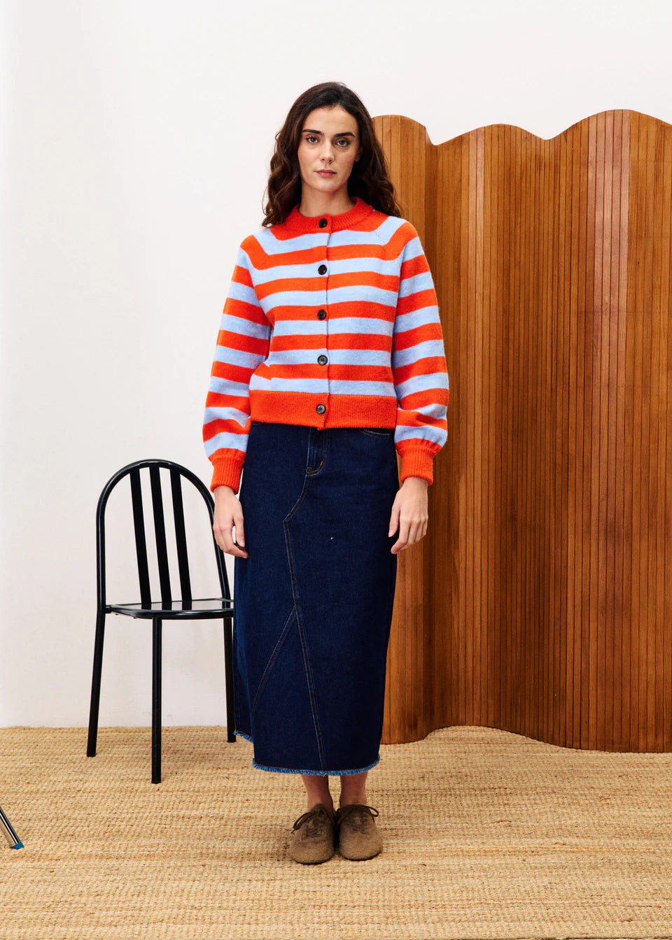 Woman wearing a red and blue striped sweater with a wooden wall and black chair in the background