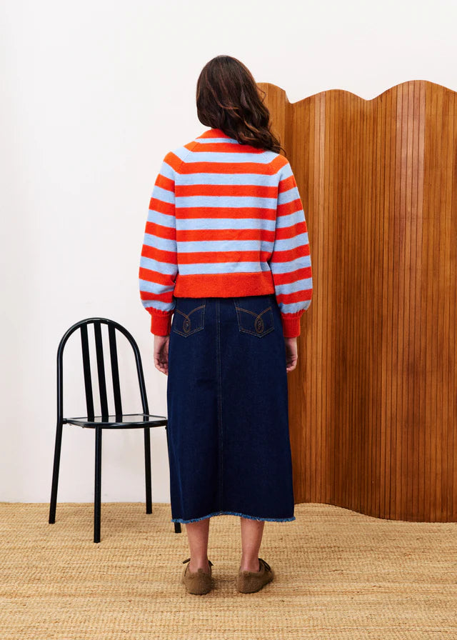 Person wearing a red and white striped sweater and blue skirt standing in front of a wooden screen.