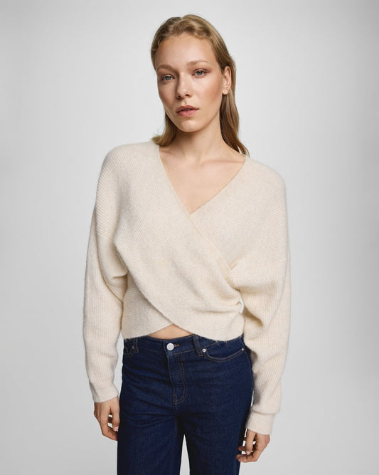 Woman wearing a beige sweater and blue jeans on a plain background